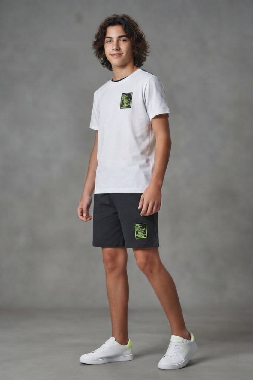 Niño con remera blanca con parche y short negro con parche verde, zapatillas blancas